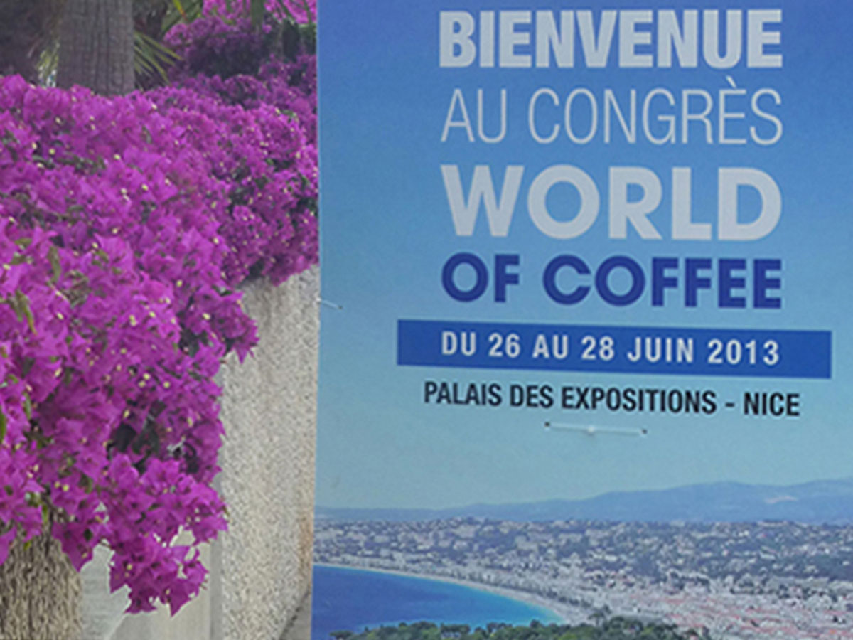 Welcome sign beside bougainvillea bush at World of Coffee in Nice, stating 'Bienvenue au congress WORLD OF COFFEE Palais des Expositions