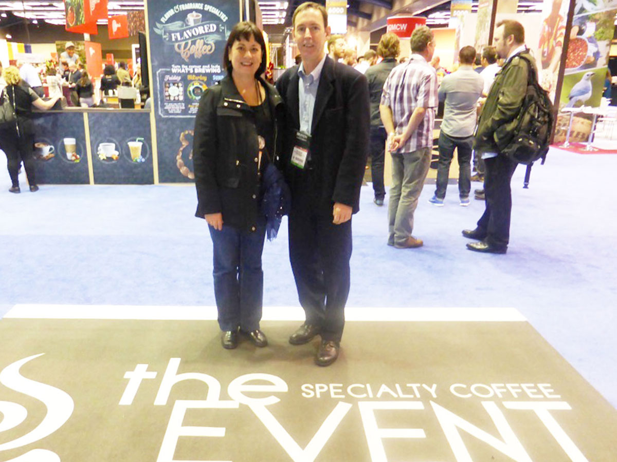 Christine Cottrell and Paul Holiday standing on a mat with the sign saying Specialty Coffee Event in Seattle 2014