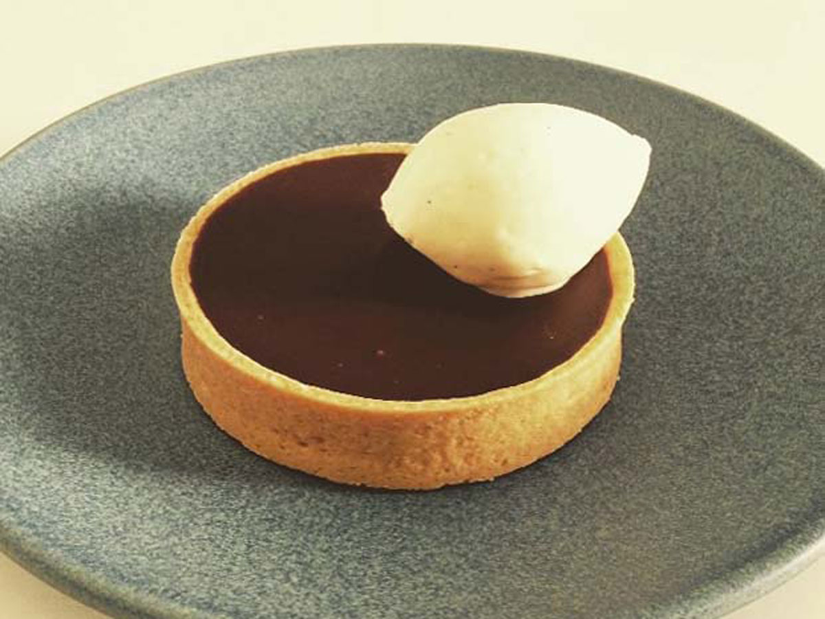 Chocolate ganache tart with a dollop of cream on the right hand side and served on a sage green stoneware plate at Little May Espresso in Montville.