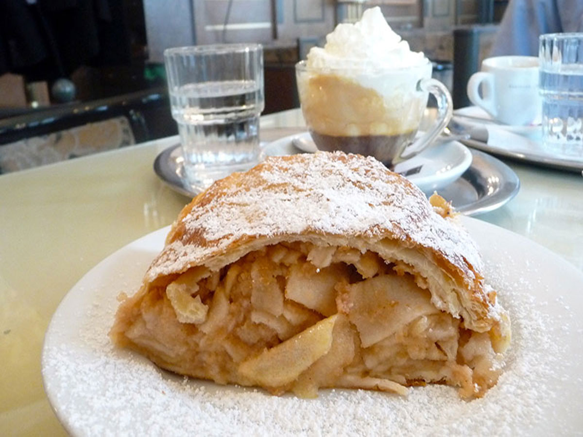 Viennese apple strudel served with coffee and cream with a cup of Vienna Coffee piled high with cream in the background