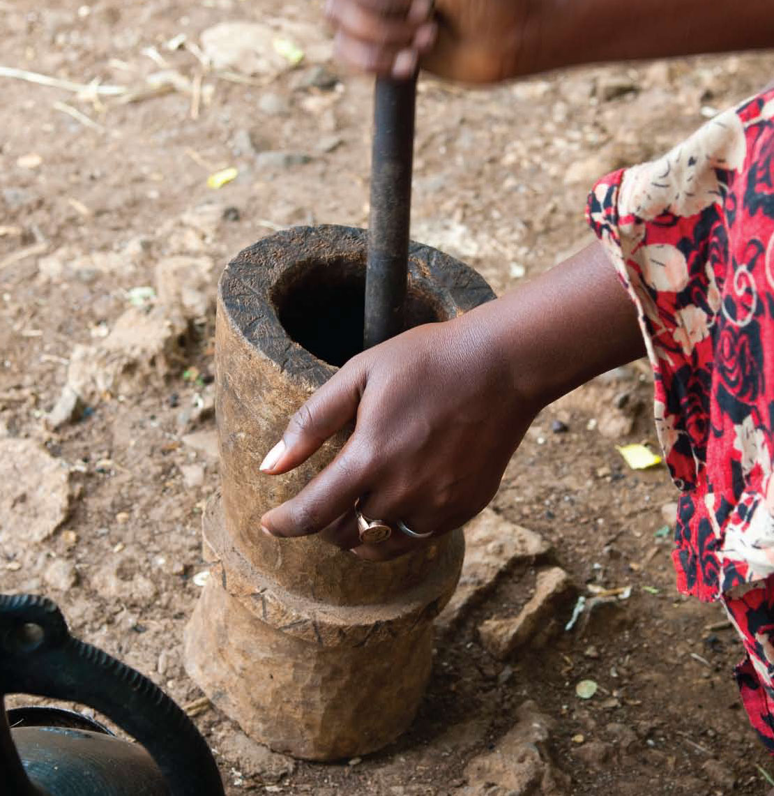 mage of a woman with dark skin grinding coffee beans in a pot on the ground