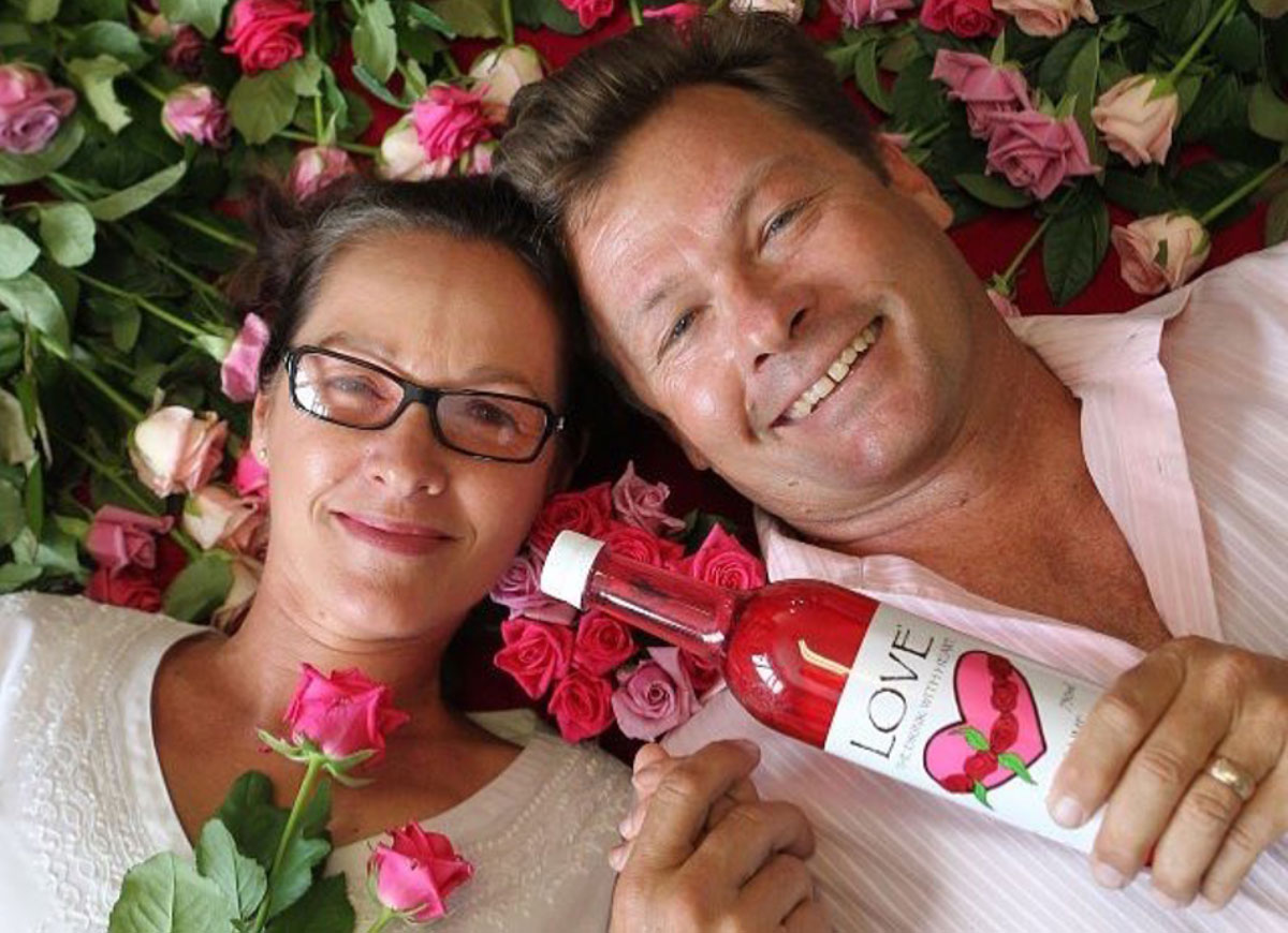 A man and a lady lying in a bed of roses, holding a bottle of pink cordial with LOVE on the label