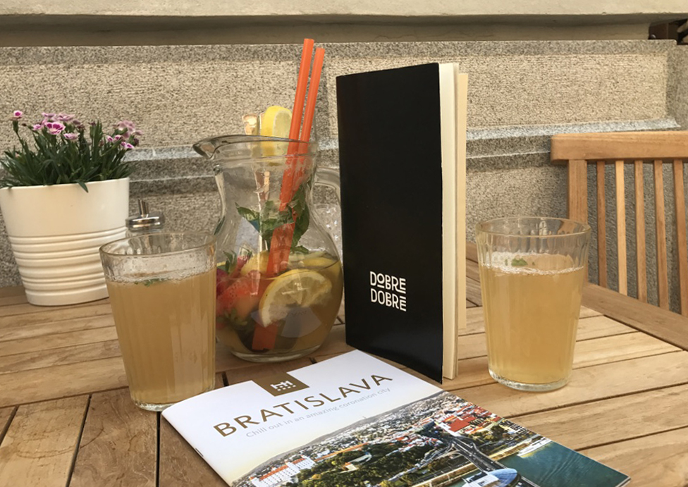 At Dobre Dobre Cafe in Bataslava, a menu is sitting on a table with a tourist guide, a carafe and two glasses with a beverage, and a pot of flowers