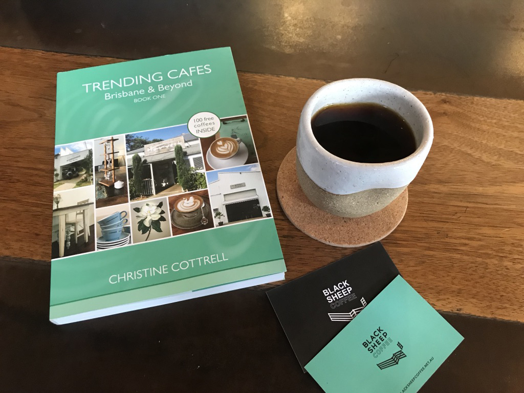 The Trending Cafes book sitting on a table next to a cup of coffee at Black Sheep Coffee in Woollongabba