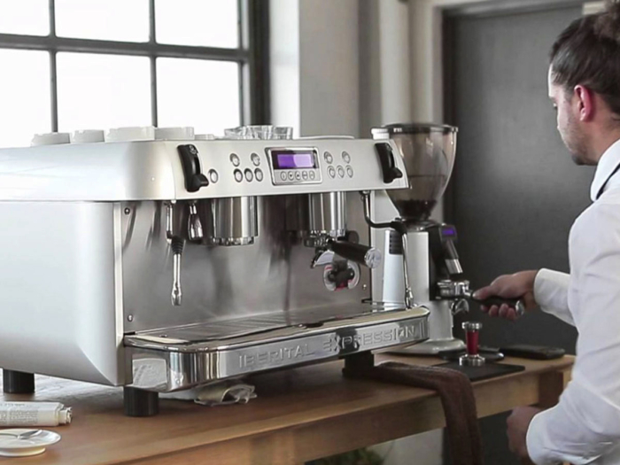 Iberital espresso machine and Compak grinder with a young barista in a white shirt dosing a filter basket.