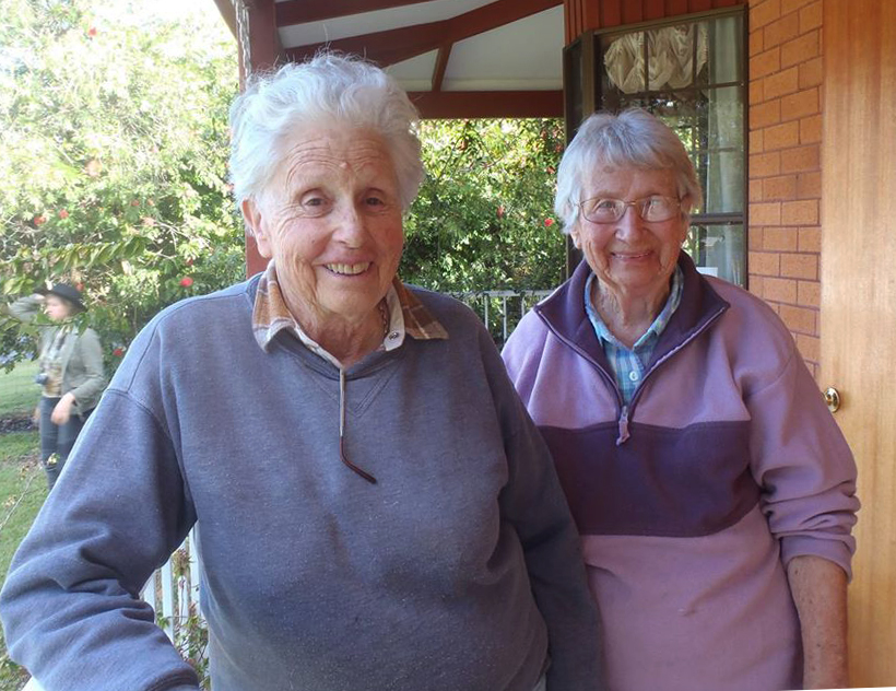 Joan Dibden and Joy Phelps pioneering coffee growers standing on the patio outside a red brick house at their Wombah Coffee Plantation