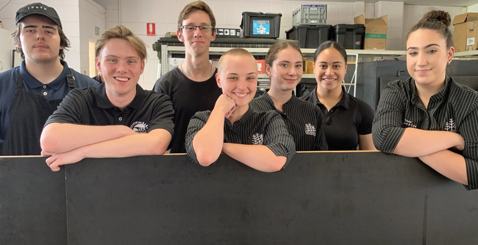 7 young people smiling leaning over a blackboard