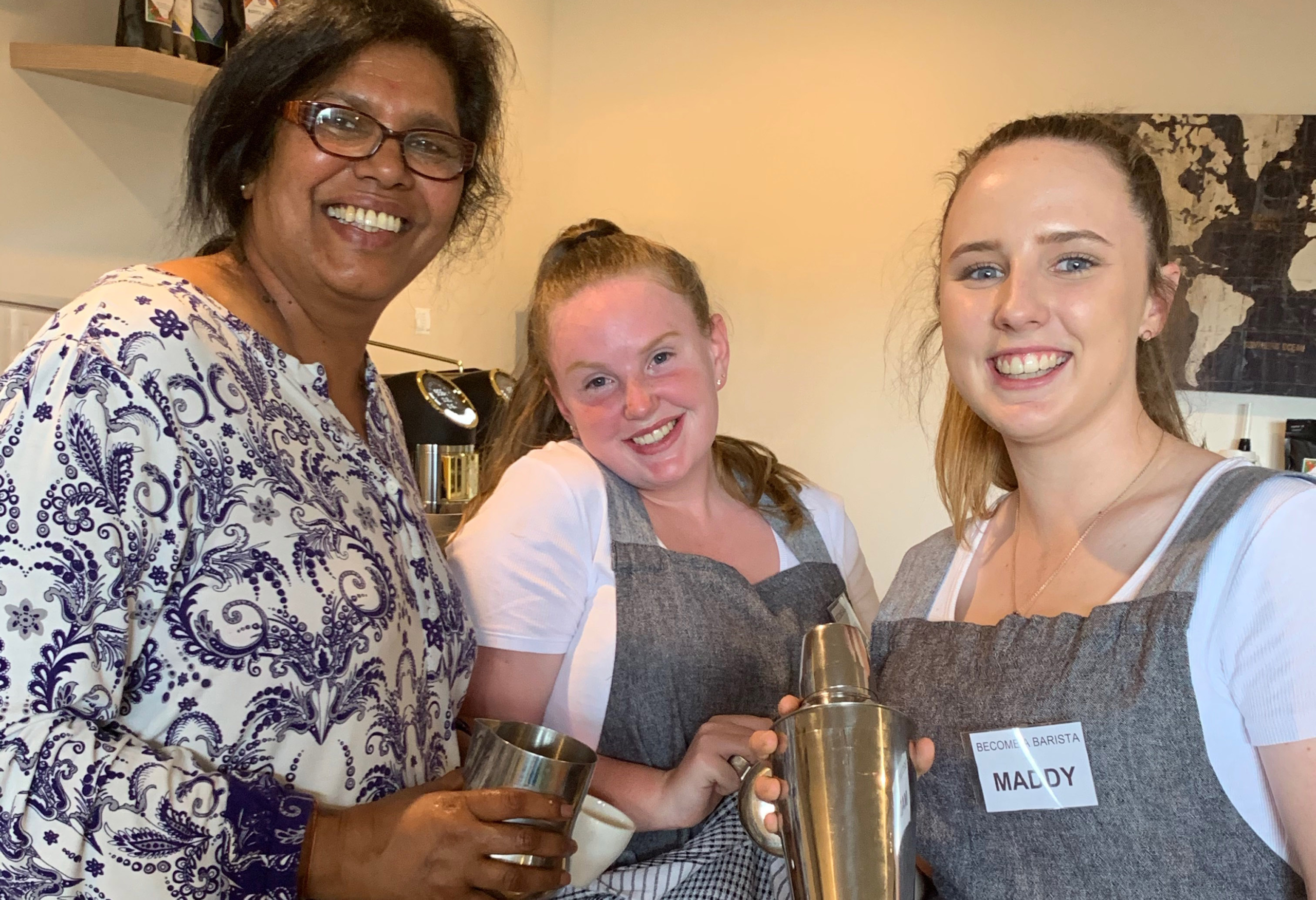 A woman and two young girls smiling holding metal coffee making equipment