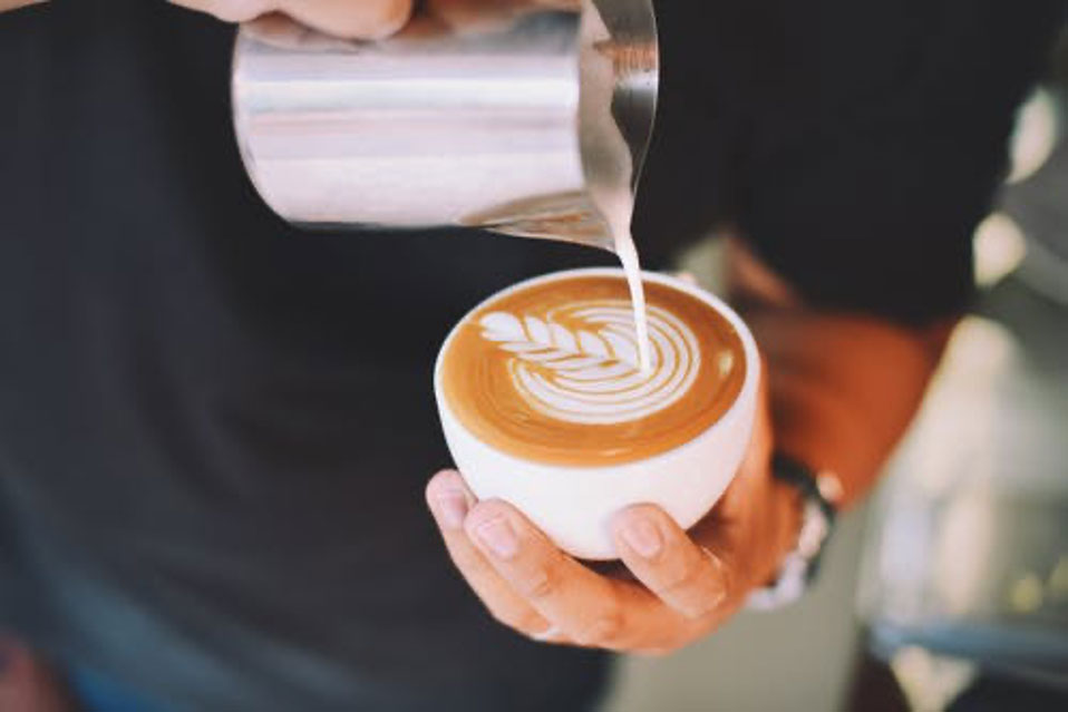 Barista pouring sa let art design holding the jug in one hand and the cup in the other.