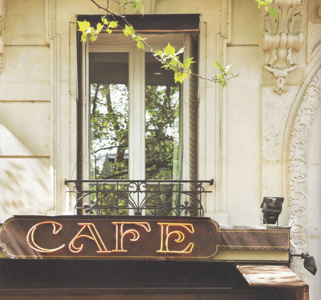 A balcony in a European cafe with leaves trailing over the windows and a Cafe sign below